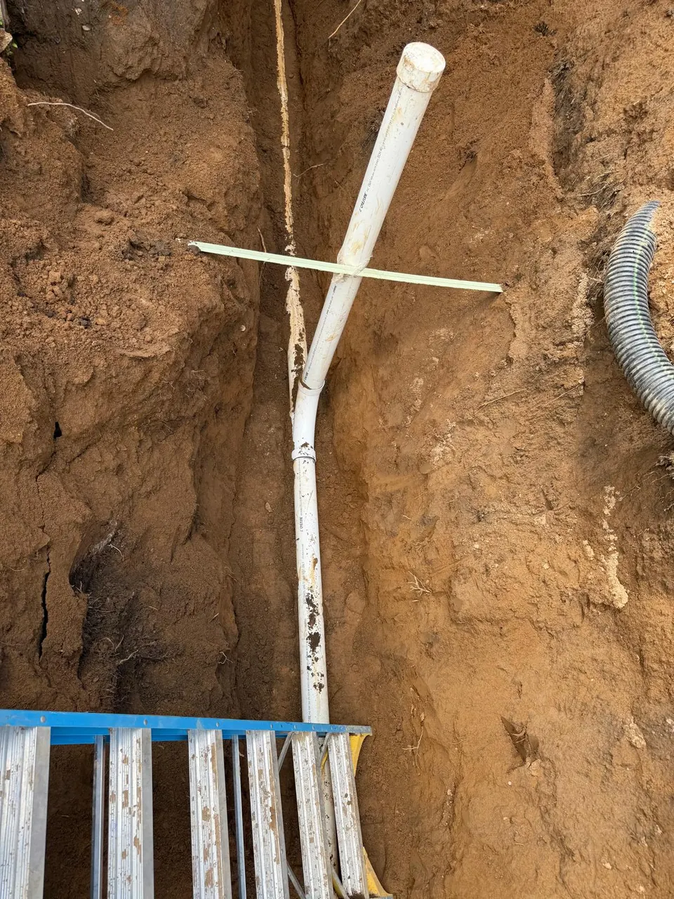Deep sewer trench with a new PVC cleanout riser and a ladder for access